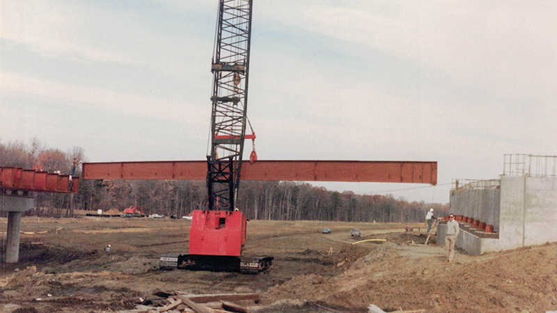 John M. Rouse contracted equipment carrying a steel girder on newly dug site work.